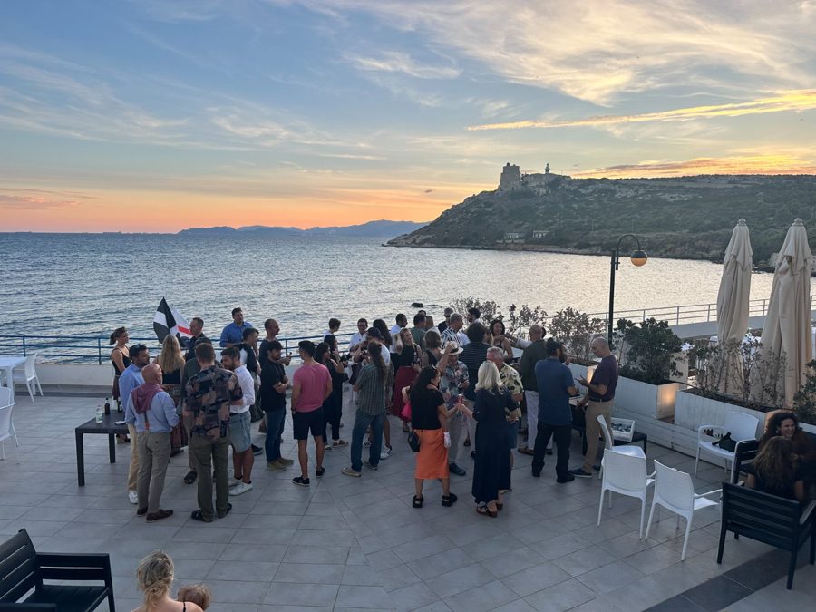 Guests gather on seaside terrace during sunset by a coastal fortress.