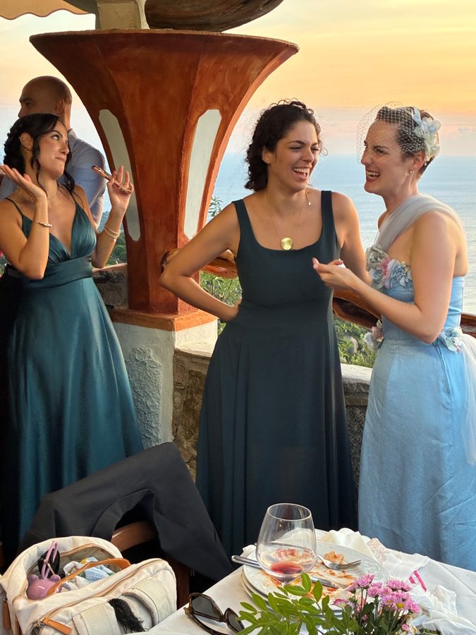 Bride laughs warmly with two female friends at outdoor dinner table.